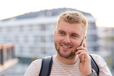 Handsome blond bearded smiling man with casual clothes,having call using smartphone in city 