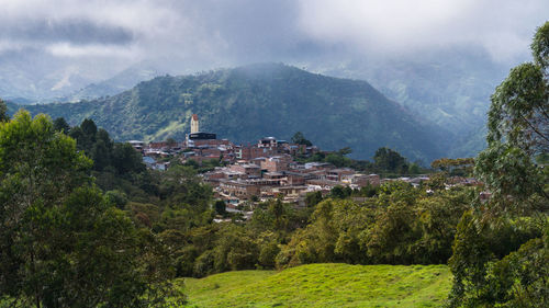 Trees and houses in town by mountains against sky