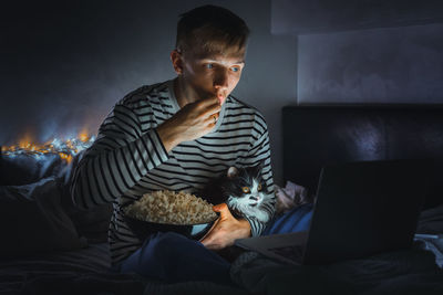 Young man watching movie with cat while eating popcorn