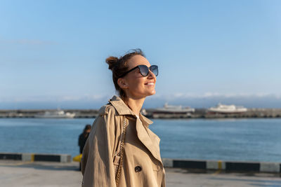 Portrait of woman wearing sunglasses while standing at beach against sky