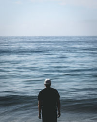 Rear view of man standing in sea against sky