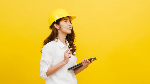 Smiling young woman using mobile phone against yellow background