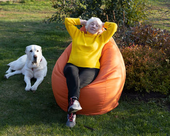 Attractive gray-haired 85 year old woman sits on a bag chair and listens to music on headphones.