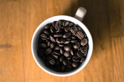 Directly above shot of roasted coffee beans in cup on hardwood floor