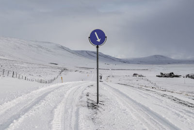 Road sign on snow covered landscape against sky