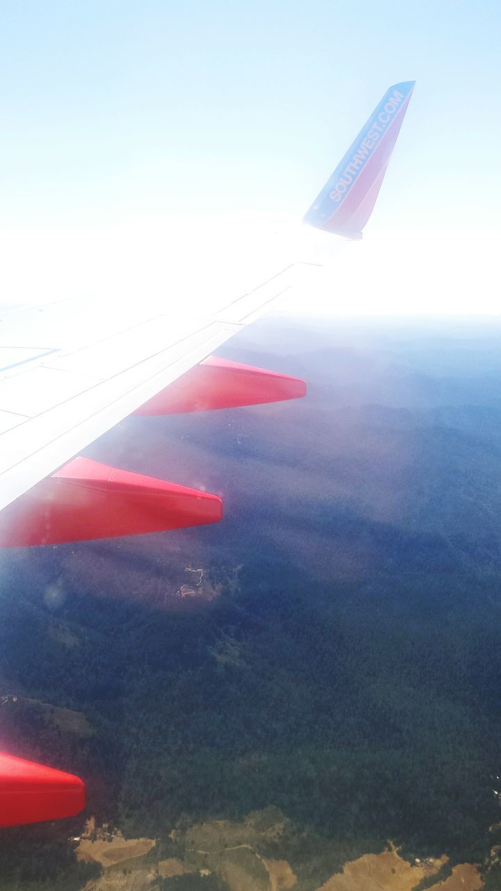 transportation, flying, air vehicle, mode of transport, airplane, aircraft wing, mid-air, travel, part of, on the move, landscape, journey, clear sky, aerial view, flag, blue, cropped, sky, day, no people