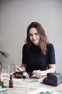 Portrait of smiling brunette eating lunch against wall at workshop