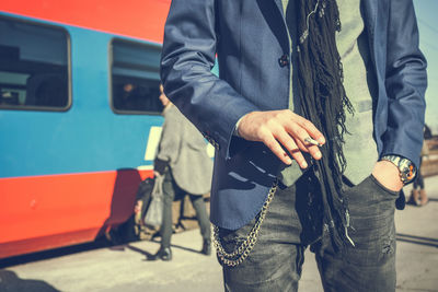 Midsection of man holding cigarette at railroad station platform