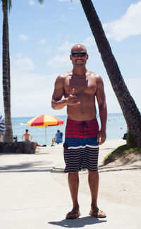 Full length of shirtless man standing at beach against sky