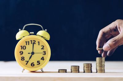 Cropped hand stacking coins by alarm clock on table