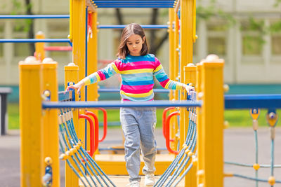 Little cute girl 5-6 years old on a childrens ladder on a bright yellow playground