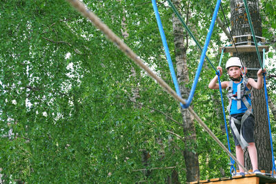 Child boy having summer fun at adventure park on the zip line. balance beam and rope bridges