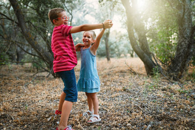 Full length of siblings dancing on land in forest