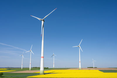 Windmills on field against clear blue sky