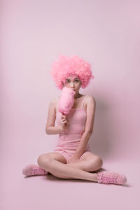 Portrait of woman sitting against pink background