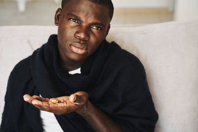 Portrait of man holding medicine sitting on sofa at home