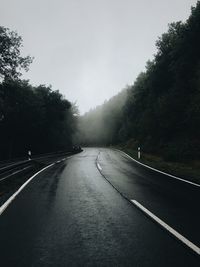 Empty road amidst trees against sky