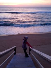 High angle view of woman standing on steps at beach during sunset