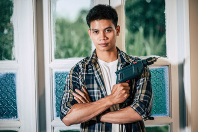 Portrait of young man standing against window