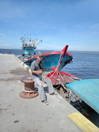 Man sitting on bollard by sea