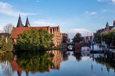 Reflection of trees and buildings on river against sky