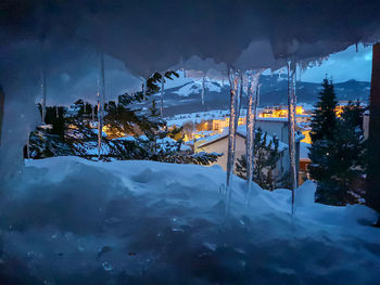 Icicles in cave against illuminated townscape at dusk