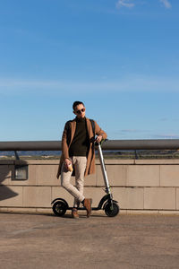 Vertical view of young bussinesman resting  enjoying a cup of coffee outdoors with electric scooter