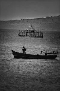 Fisherman standing in fishing boat in sea against sky