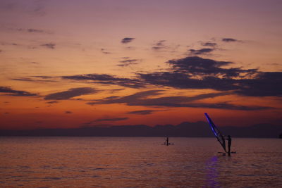 Scenic view of sea and windsurfing against sky during sunset