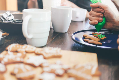 Cropped hand of person icing cookies on table