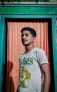 Young man looking away while standing against wall