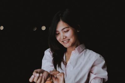 Smiling young woman standing against black background