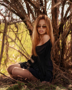 Young woman wearing sunglasses while sitting by tree in forest