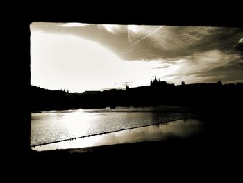 Silhouette buildings by river against sky