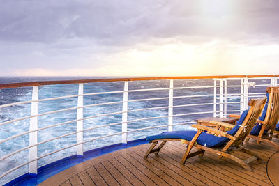 Chairs on railing by sea against sky