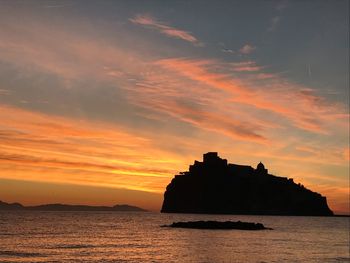 Silhouette rocks on sea against sky during sunset