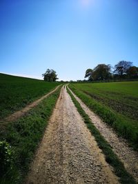 Road amidst field against clear sky