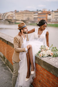 Newlywed couple sitting on retaining wall by canal