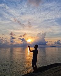 Silhouette man standing in sea against sky during sunset