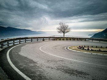 Empty road by trees against sky