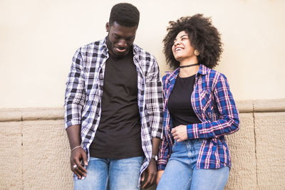 Smiling young couple standing against wall outdoors