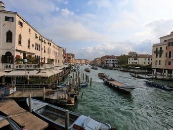 Boats moored on canal amidst buildings in city against sky