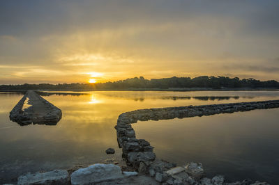 Rocks by lake against sky during sunset