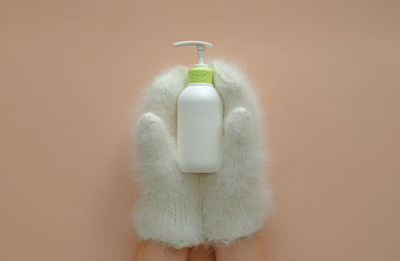 Cosmetic pump bottle of moisturizing lotion hold hands in mittens.hand skin care lotion in winter.