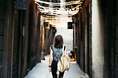 Rear view of woman carrying backpack while walking on street amidst buildings