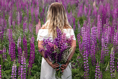 Woman standing by purple flowering plants on field