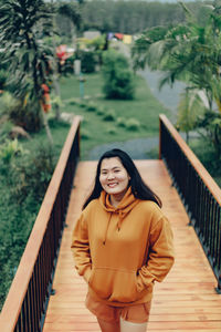 Portrait of young woman standing against bridge