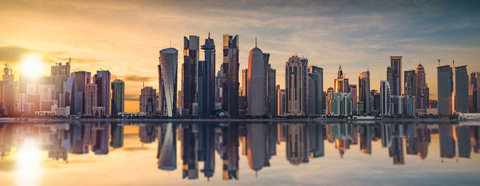 Panoramic view of city skyline reflecting on bay during sunset