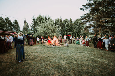 People around bonfire on field against trees