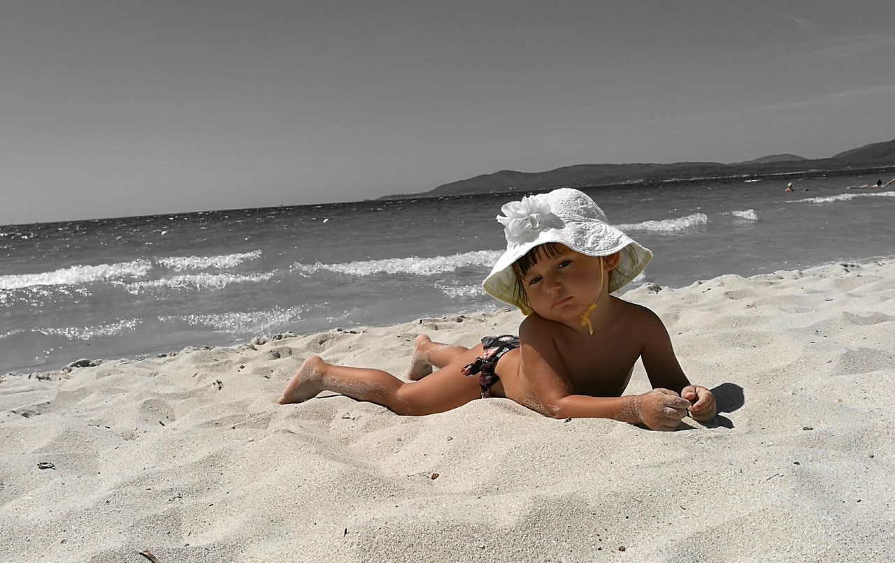 REAR VIEW OF WOMAN SITTING ON BEACH AGAINST SKY